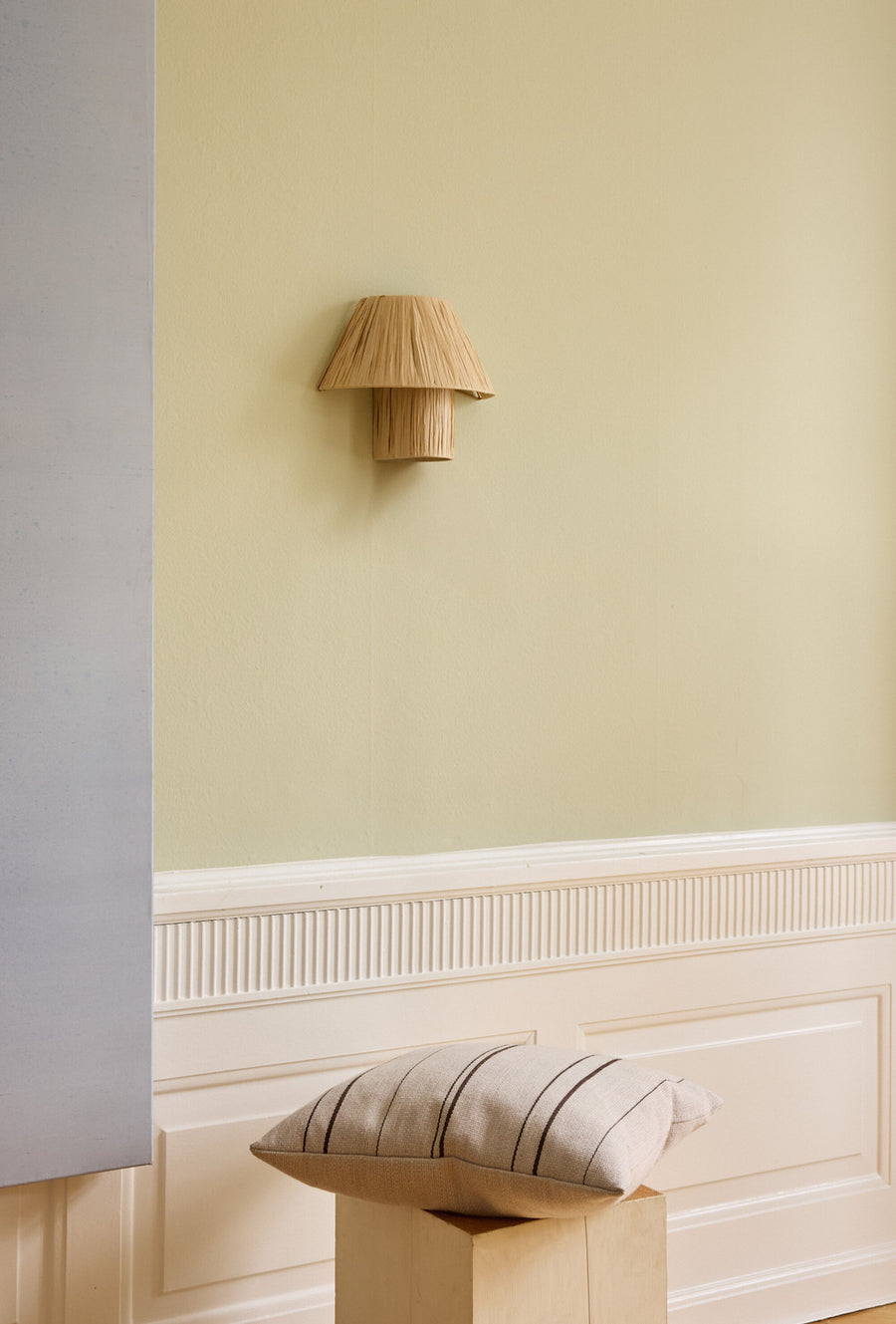 Applique murale éteinte fixée sur un mur jaune pâle au-dessus d'un coussin.