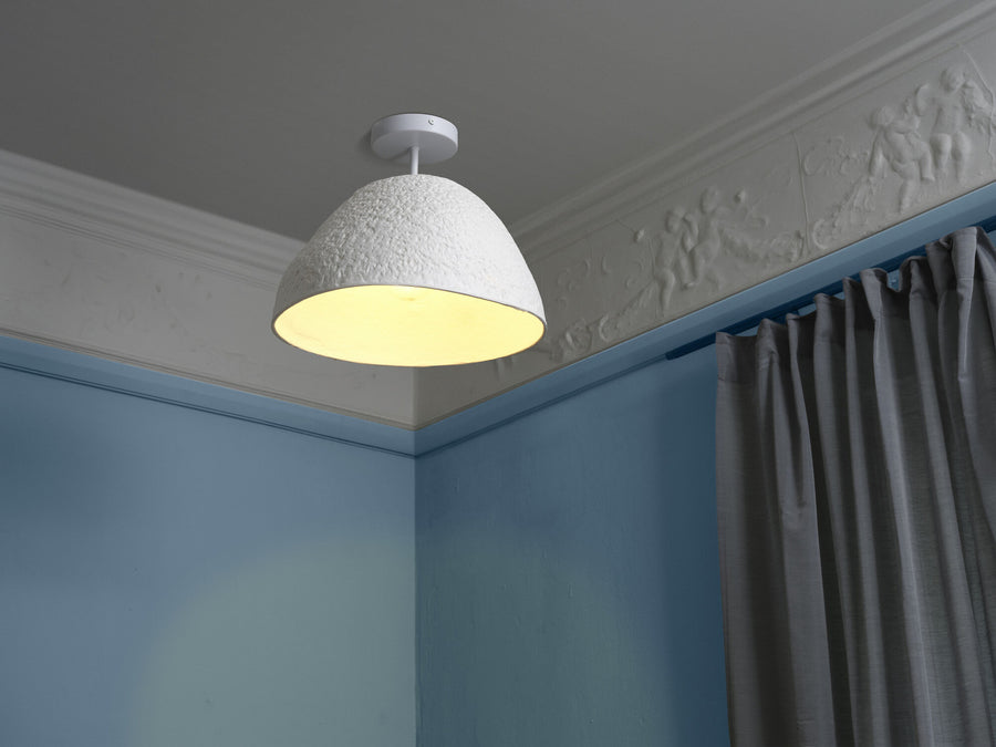 Plafonnier blanc allumé dans un angle de pièce bleue, près d'un rideau gris.