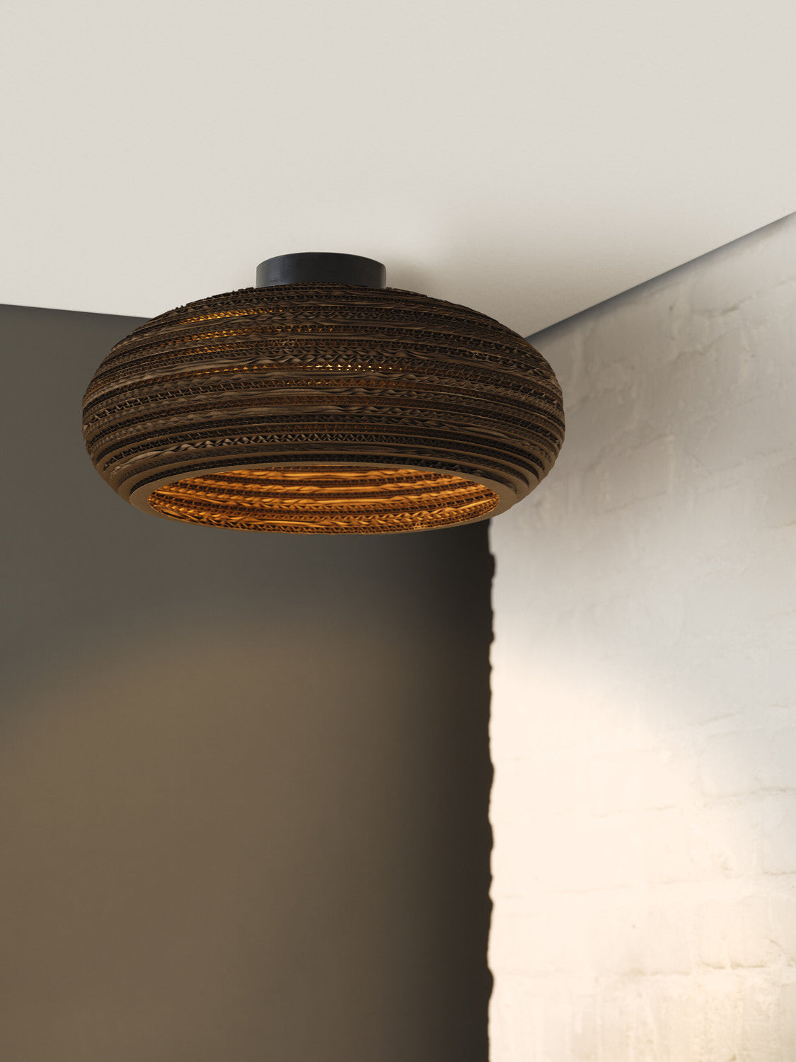Vue rapprochée du plafonnier en carton, motif ondulé et lumière chaude.