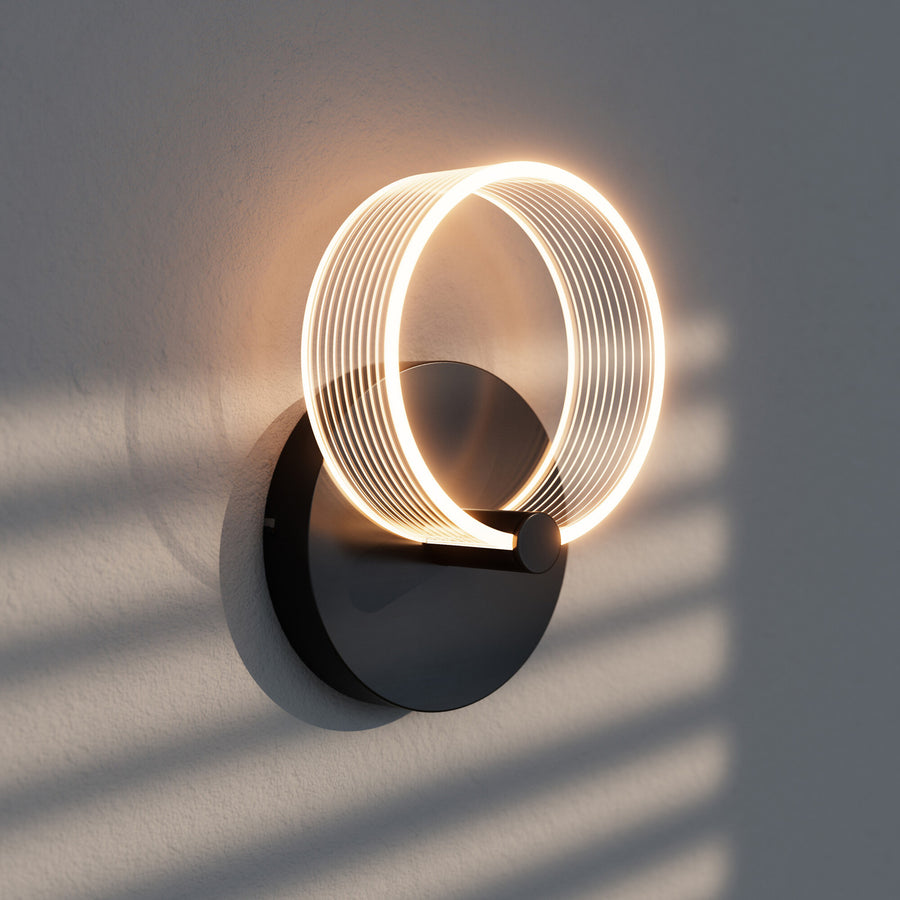 Gros plan de l'applique allumée sur mur gris, ombres striées et halo lumineux chaud.
