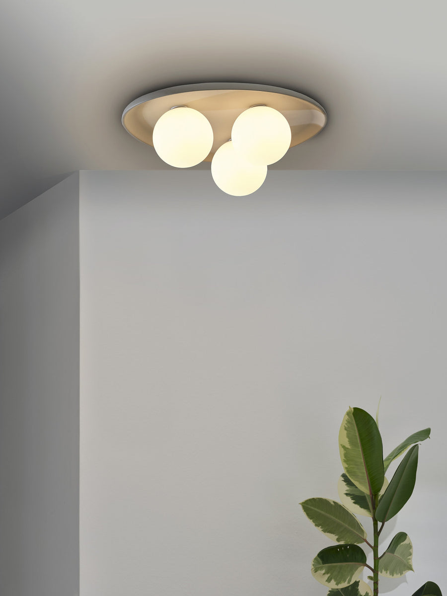 Vue rapprochée du plafonnier allumé, trois globes lumineux sous la plaque grise.