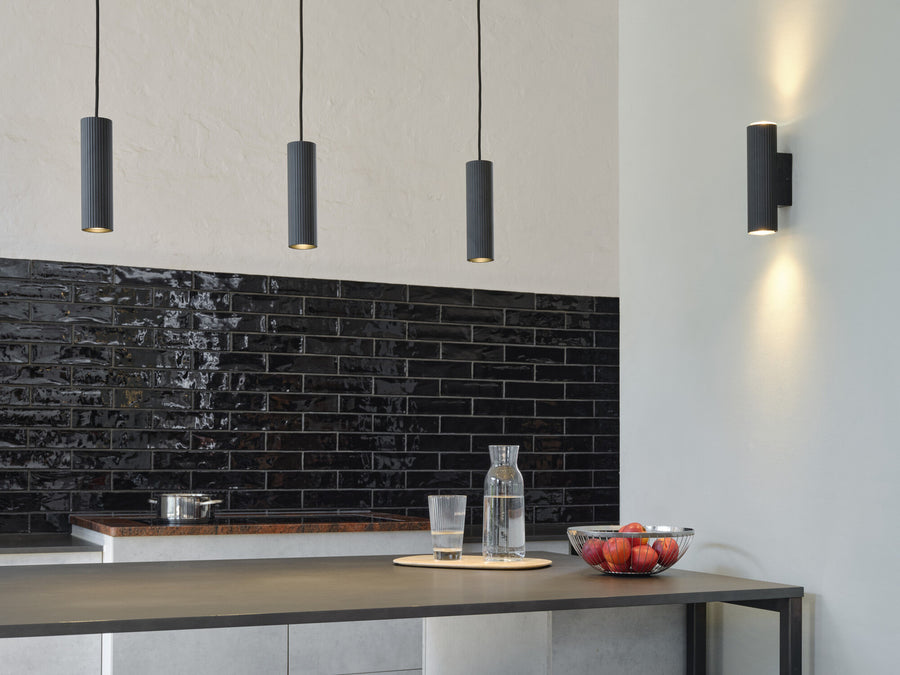 Cuisine contemporaine avec applique murale noire et suspensions cylindriques au-dessus du plan
