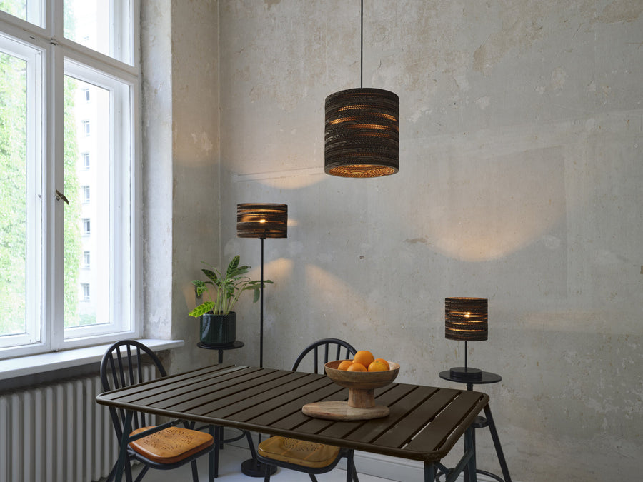 Pièce avec suspension, lampadaire et lampe à poser, table et panier de fruits.