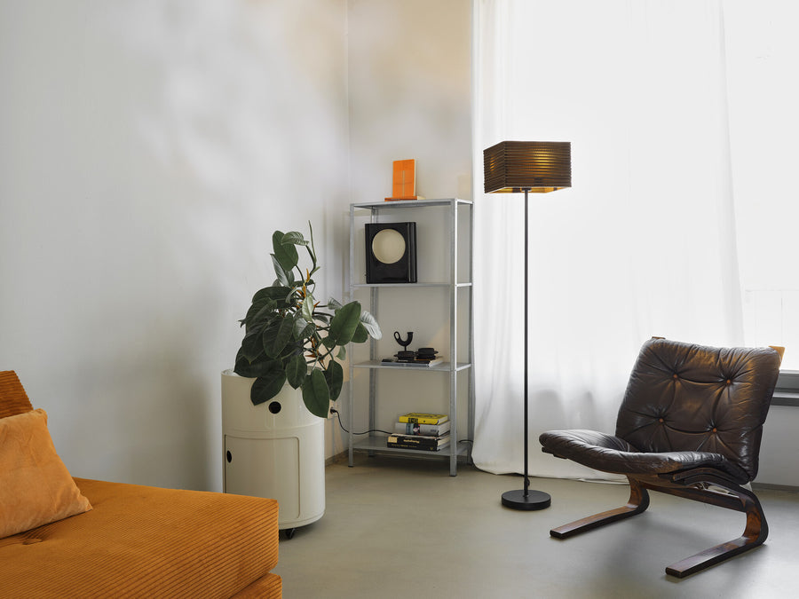 Lampadaire allumé près d'une fenêtre dans un salon avec fauteuil et plante.