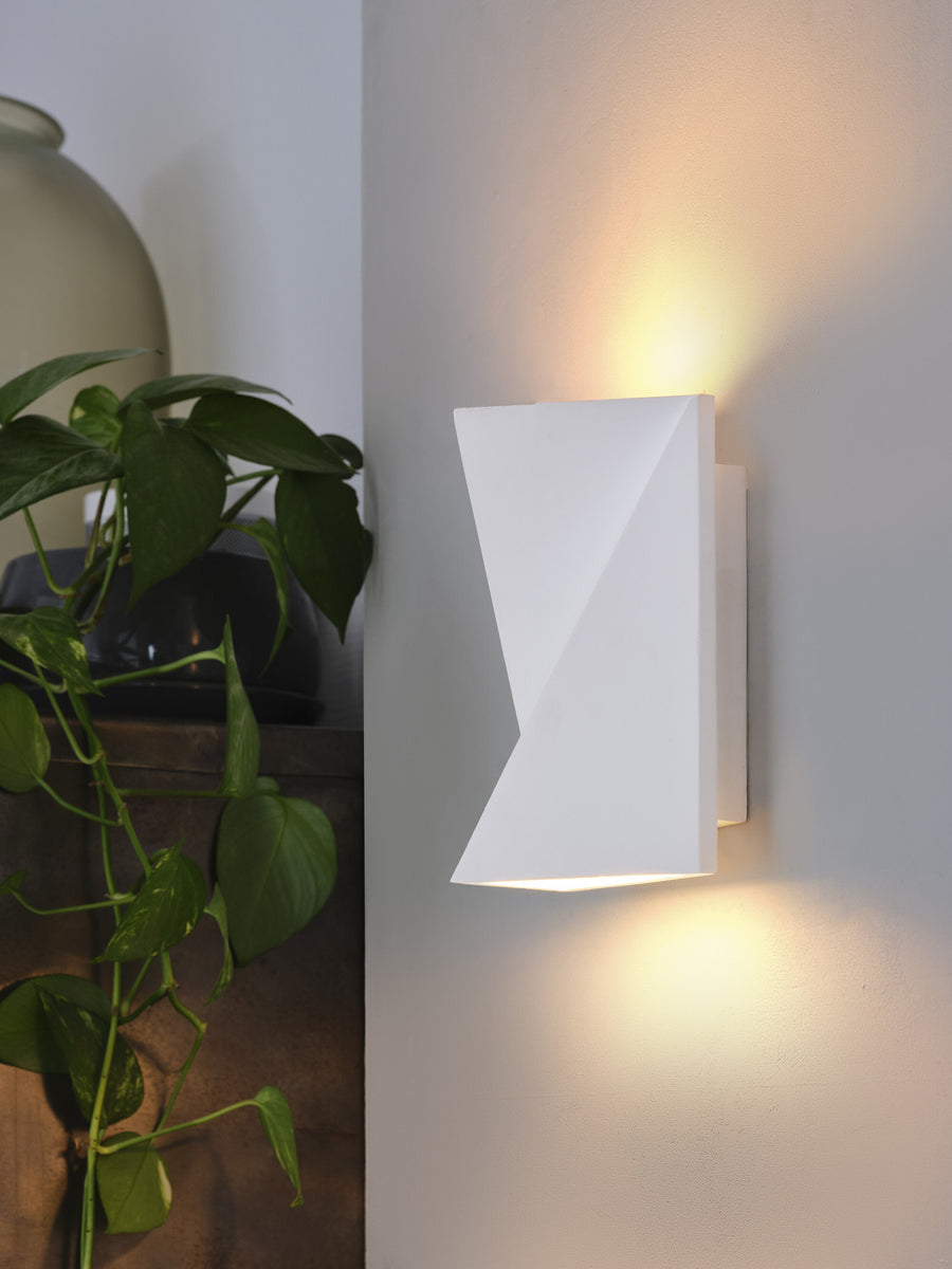 Vue rapprochée de l'applique blanche allumée près d'une plante verte et d'un vase.