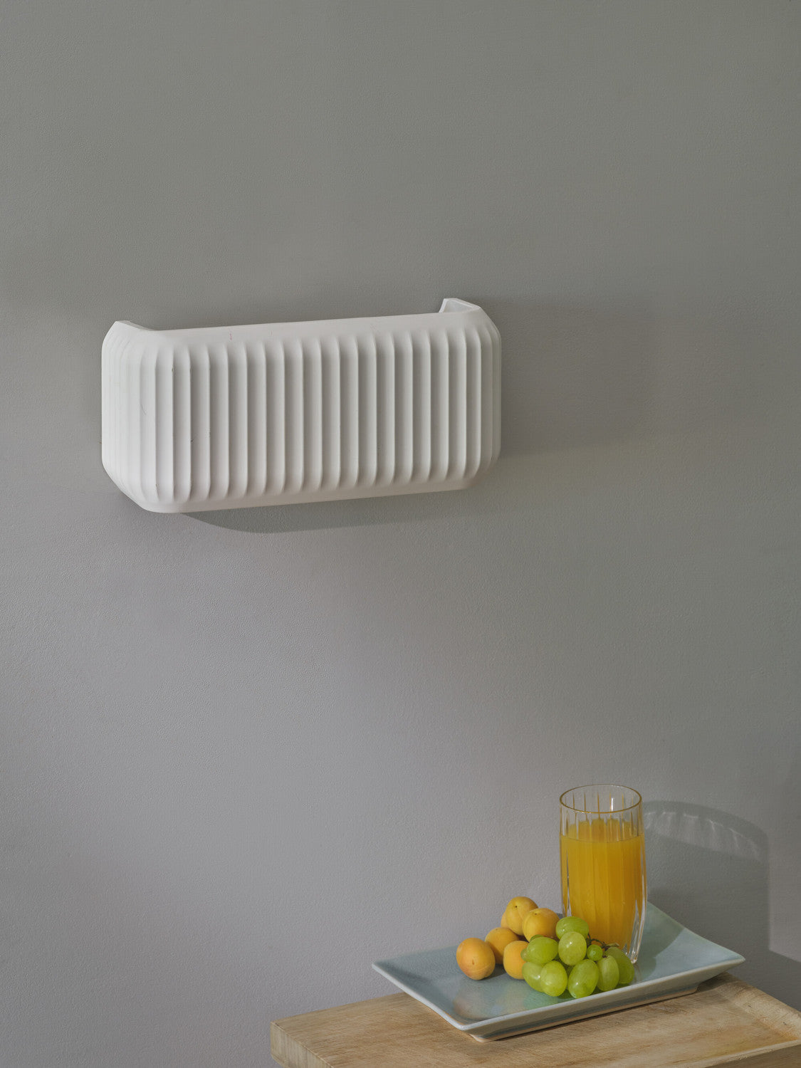 Applique murale éteinte fixée sur un mur gris au-dessus d'un plateau de fruits.