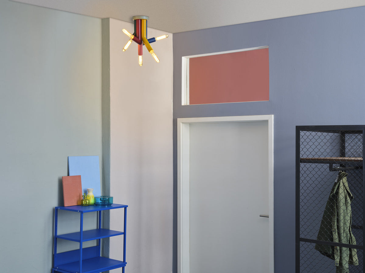 Mise en ambiance dans une entrée colorée, plafonnier allumé au-dessus d’une étagère bleue.