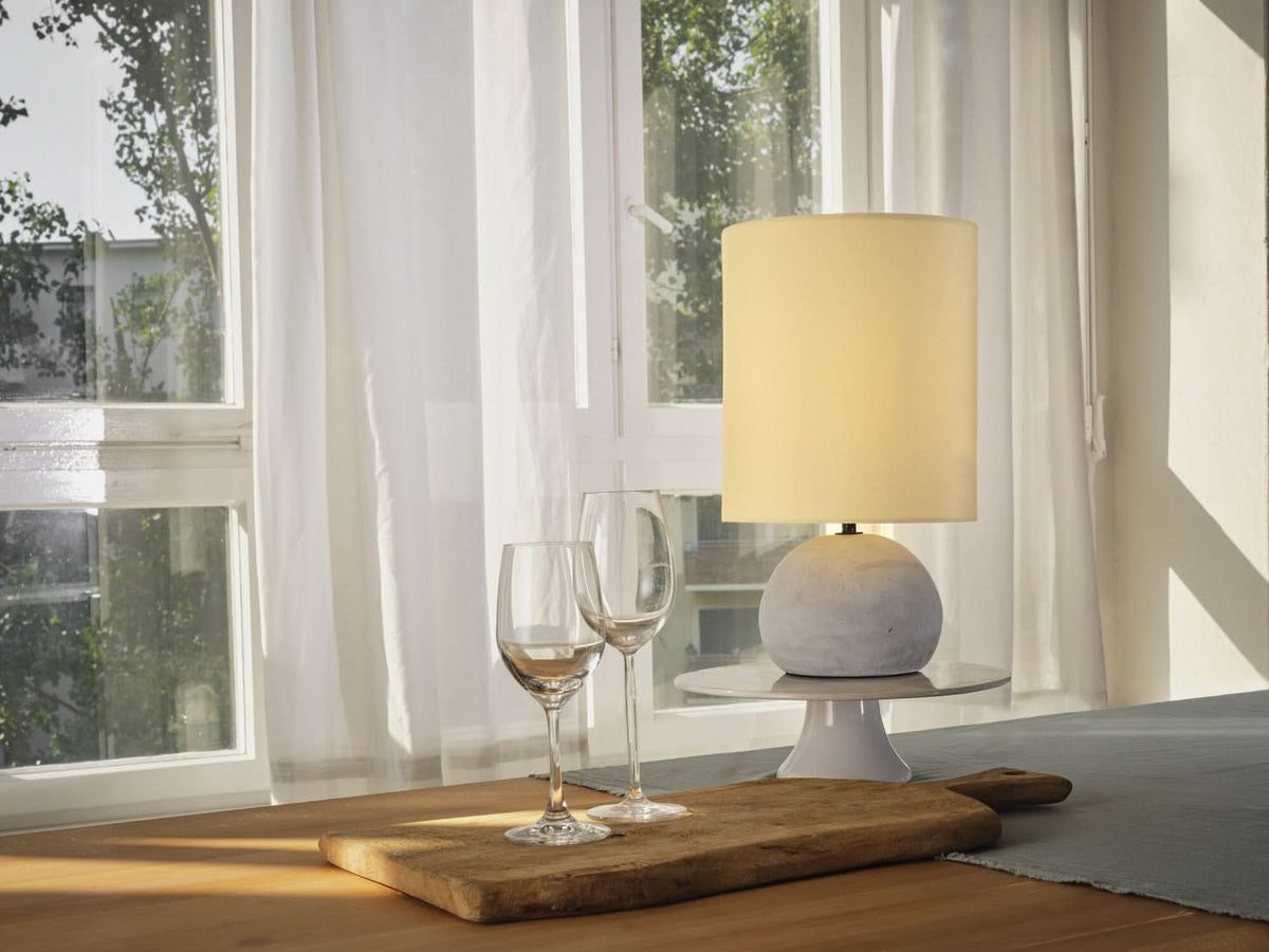 Mise en ambiance près d'une fenêtre, lampe allumée sur table en bois avec verres à vin.