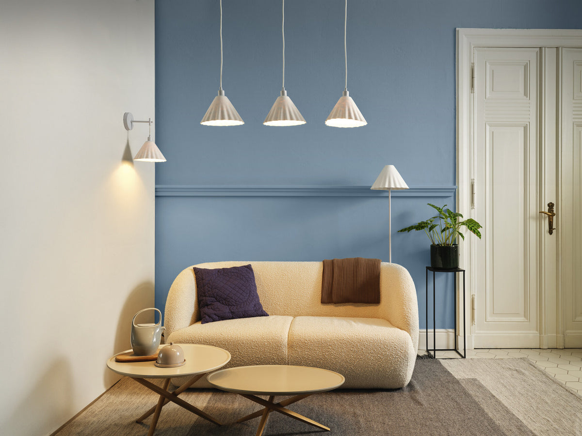 Salon bleu avec lampadaire blanc, canapé, suspensions et applique murale.