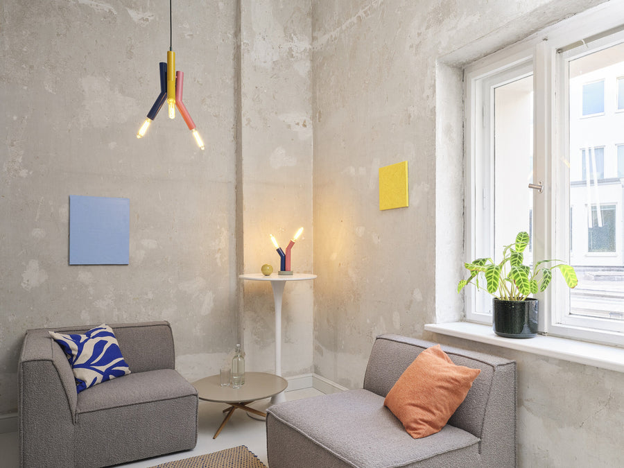Vue d'ensemble d'un salon avec suspension multicolore et lampe à poser allumée.
