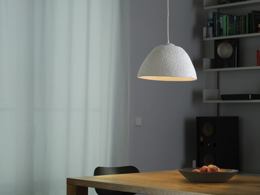 Suspension blanche suspendue au-dessus d'une table en bois devant une fenêtre et des étagères.