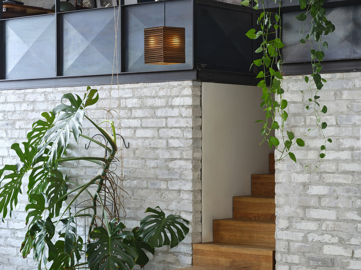 Suspension en carton allumée devant mur de briques et escalier en bois