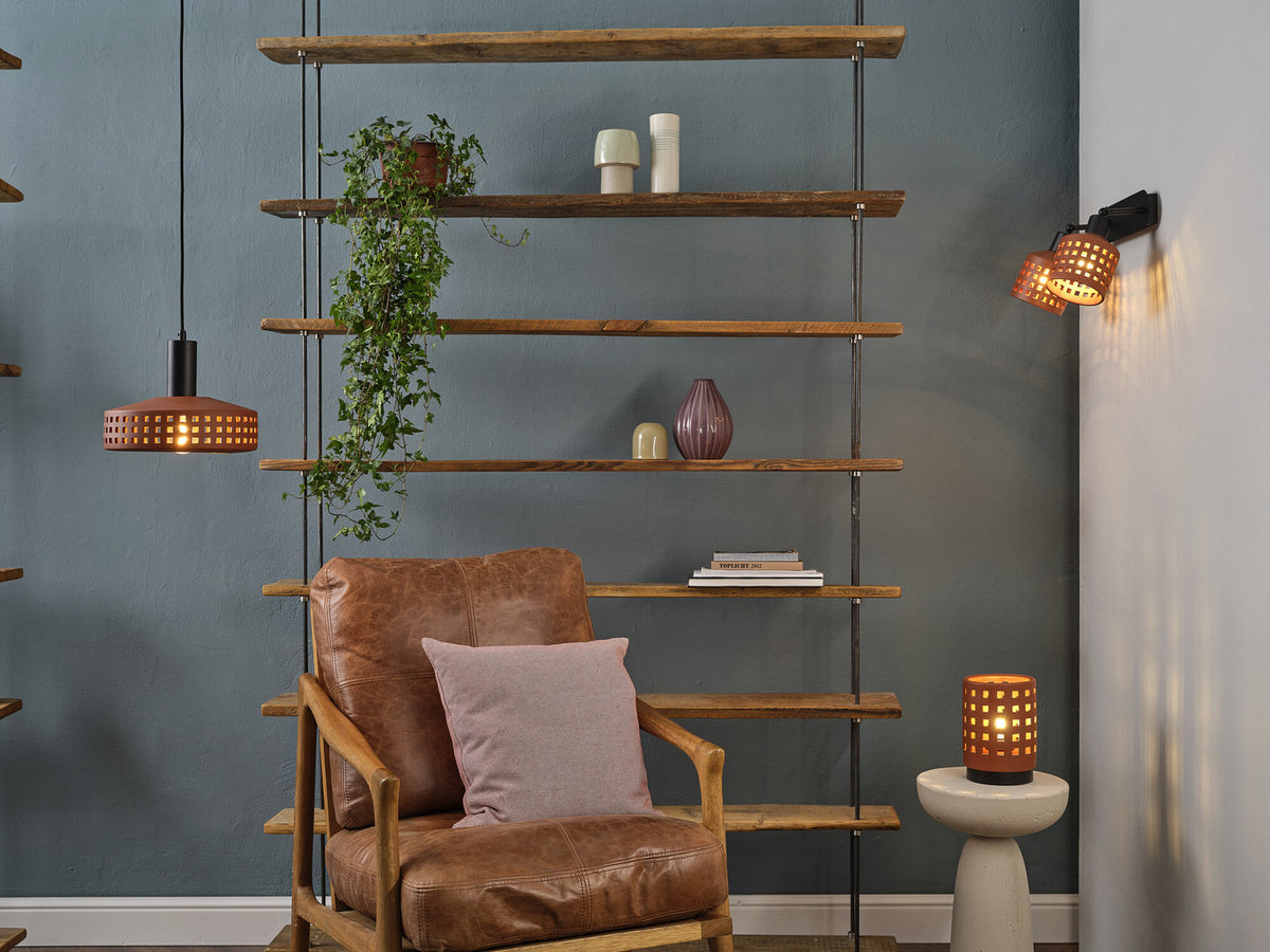 Mise en ambiance avec suspension allumée, fauteuil en cuir et étagère murale.