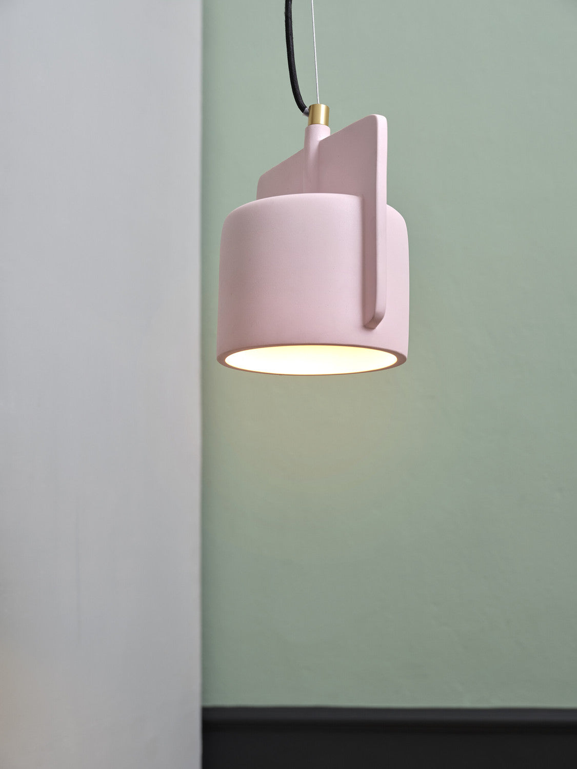 Vue rapprochée de la suspension rose allumée, ouverture lumineuse et finition béton sur fond vert.