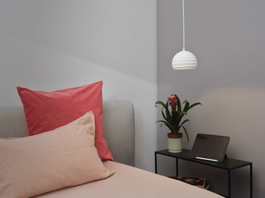 Suspension blanche suspendue dans une chambre, près d'un lit à coussins roses et plante.