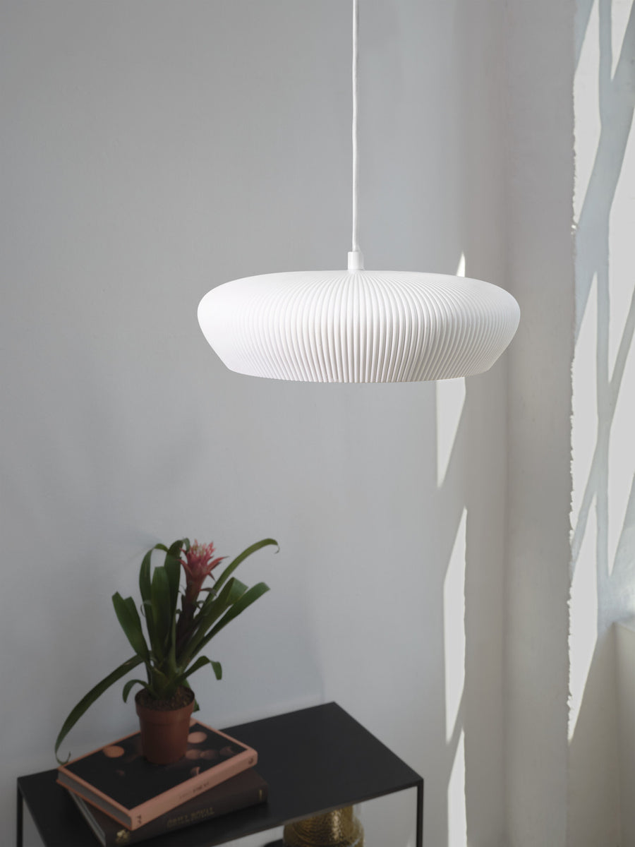 Suspension blanche suspendue au-dessus d’une plante posée sur un meuble noir.