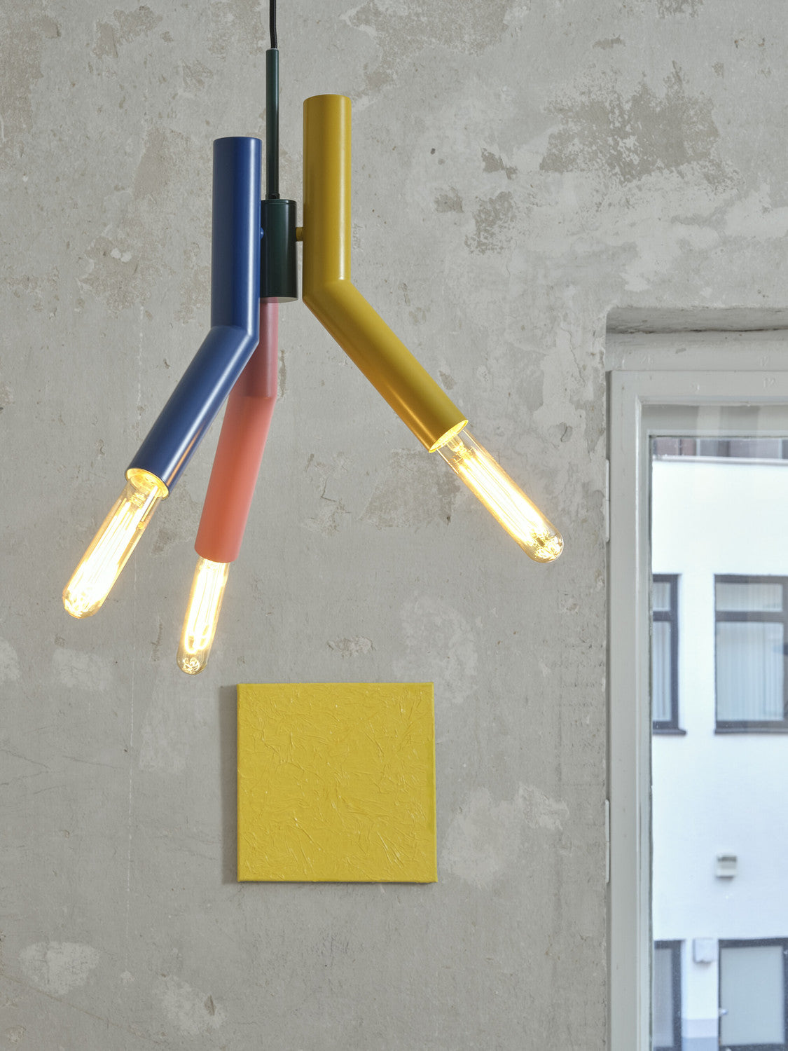 Gros plan de la suspension allumée devant un mur béton, avec ampoules filaments visibles.