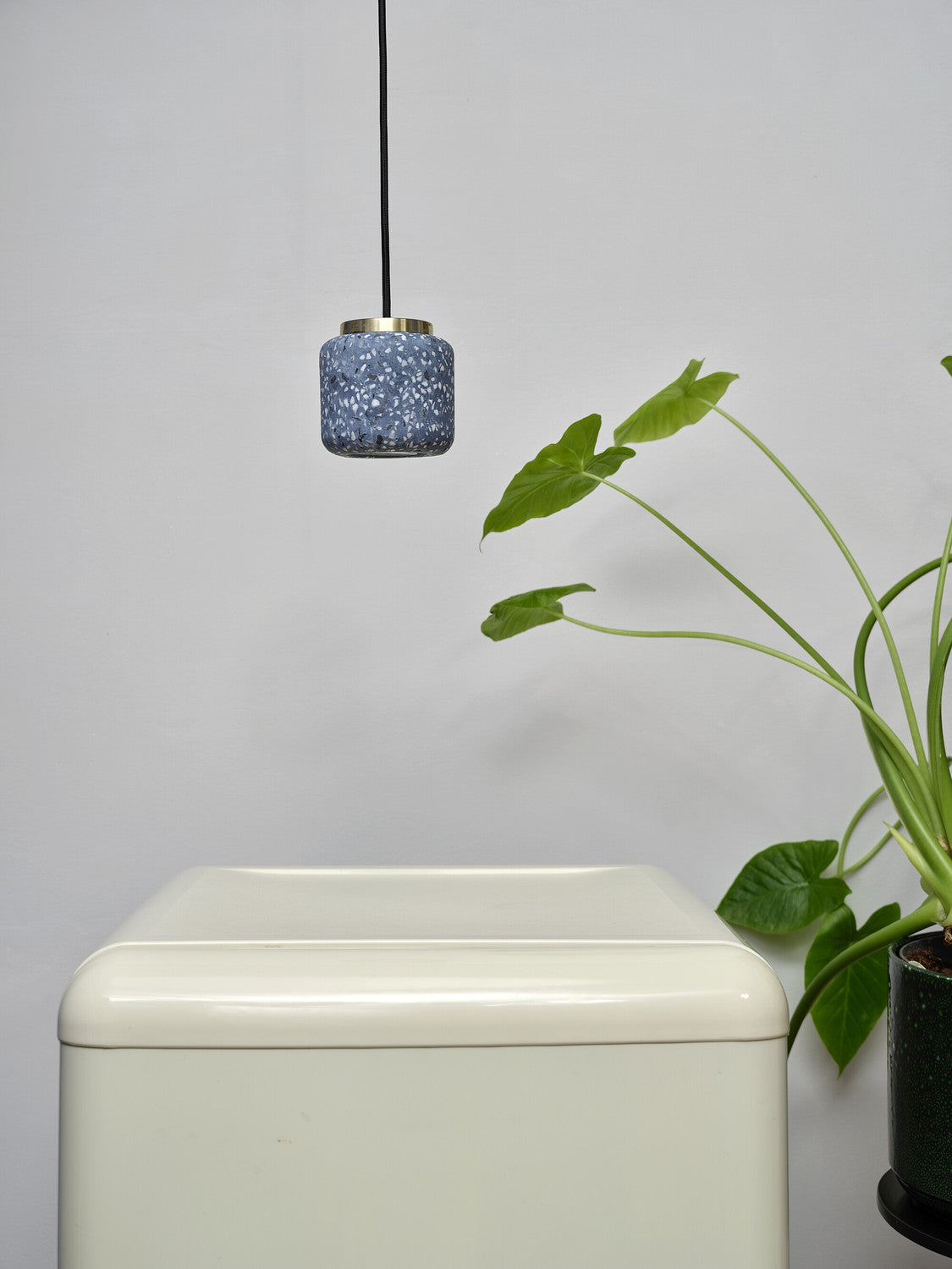 Suspension bleue installée au-dessus d'un meuble blanc près d'une plante verte