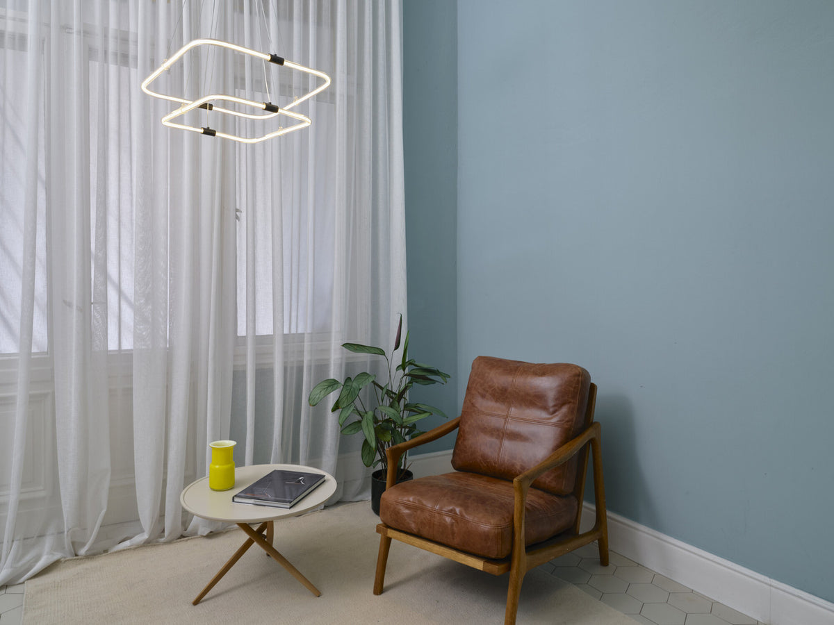 Mise en ambiance salon avec suspension lumineuse et fauteuil en cuir marron.