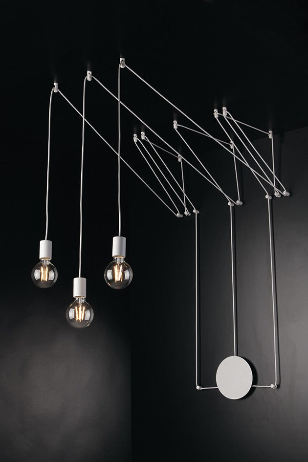 Suspension design blanc aux câbles tendus, trois ampoules et disque mural sur fond noir.