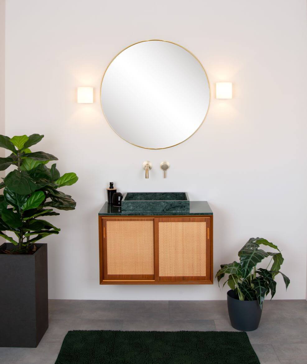 Mise en ambiance avec plantes vertes et meuble vasque en rotin sous les appliques