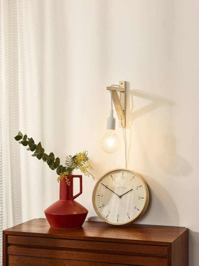 Mise en scène avec l'applique murale en bois clair, une horloge et un vase rouge.
