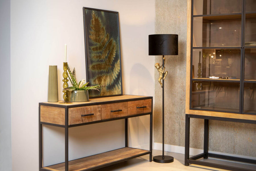 Lampadaire à singe doré devant un mur texturé et un meuble console en bois