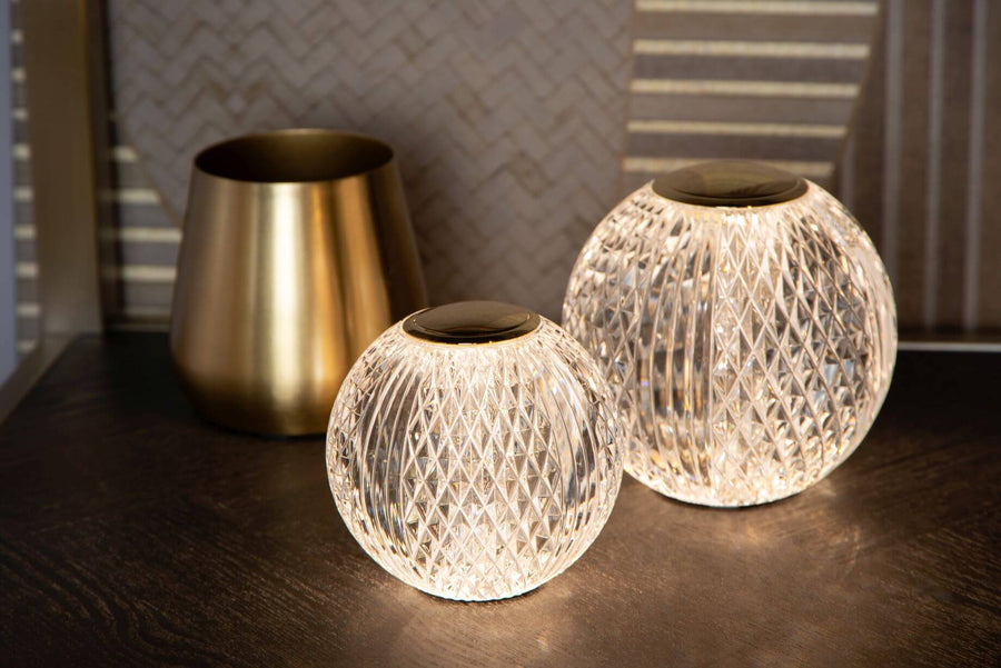 Deux lampes allumées de tailles différentes près d'un vase doré sur meuble.