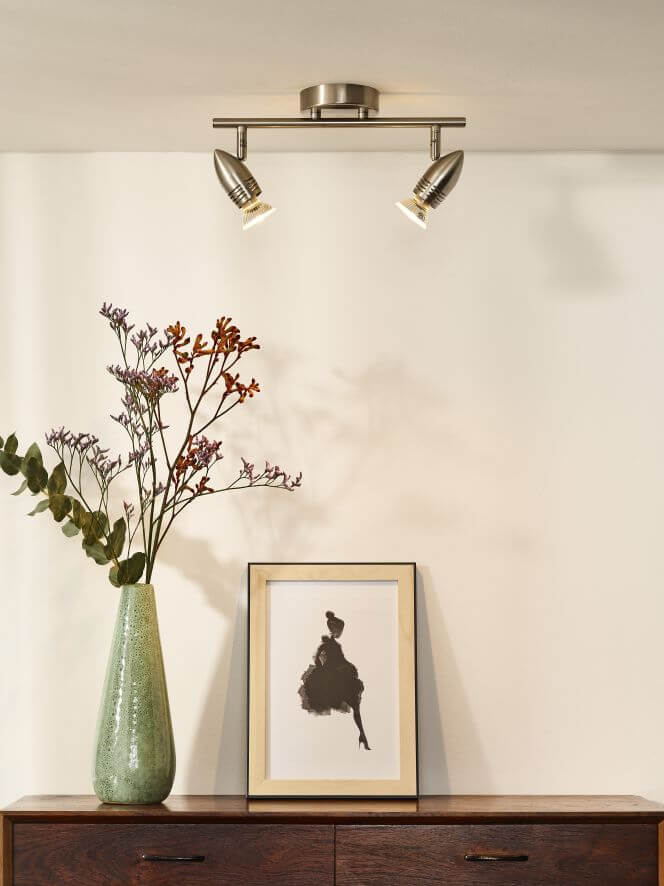 Vue rapprochée du luminaire mural chromé à deux spots orientables allumés dans un intérieur.