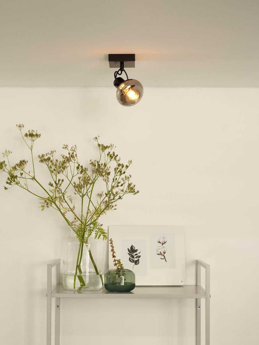 Plafonnier fixé au plafond, allumé, au-dessus d'une étagère avec vase et cadre.