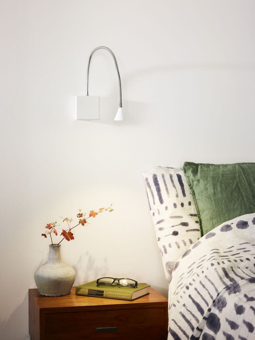 Applique murale blanche allumée au-dessus d'une table de nuit en bois dans une chambre