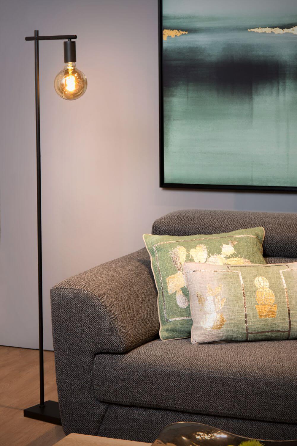 Gros plan du lampadaire noir devant un canapé gris avec coussins verts.