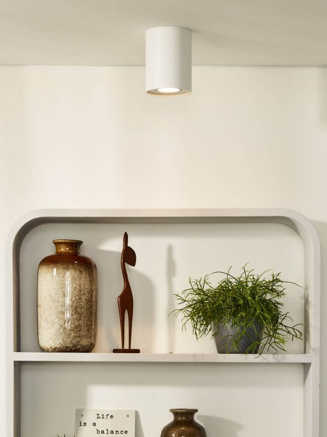 Vue rapprochée du même plafonnier blanc dans un intérieur avec étagère et plante verte.