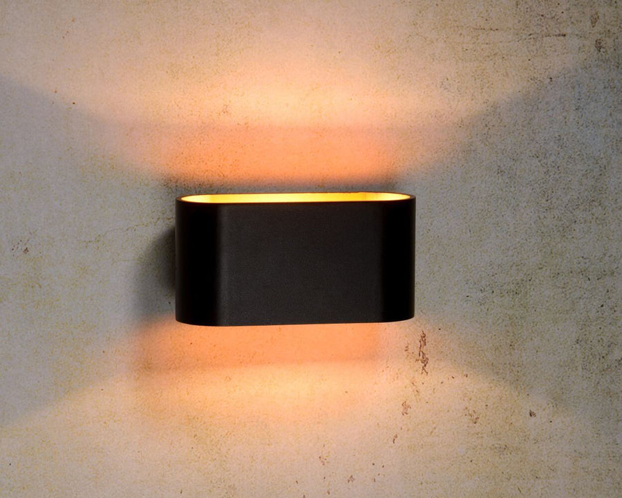 Applique murale noire allumée sur un mur texturé, halo lumineux vers le haut et le bas.