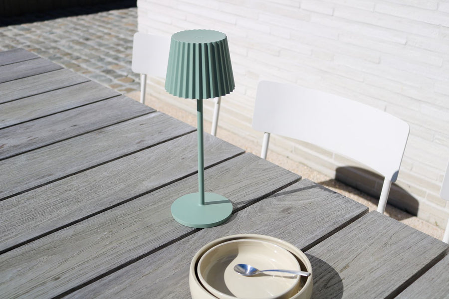 Vue rapprochée du luminaire vert sur table extérieure, assiettes empilées devant