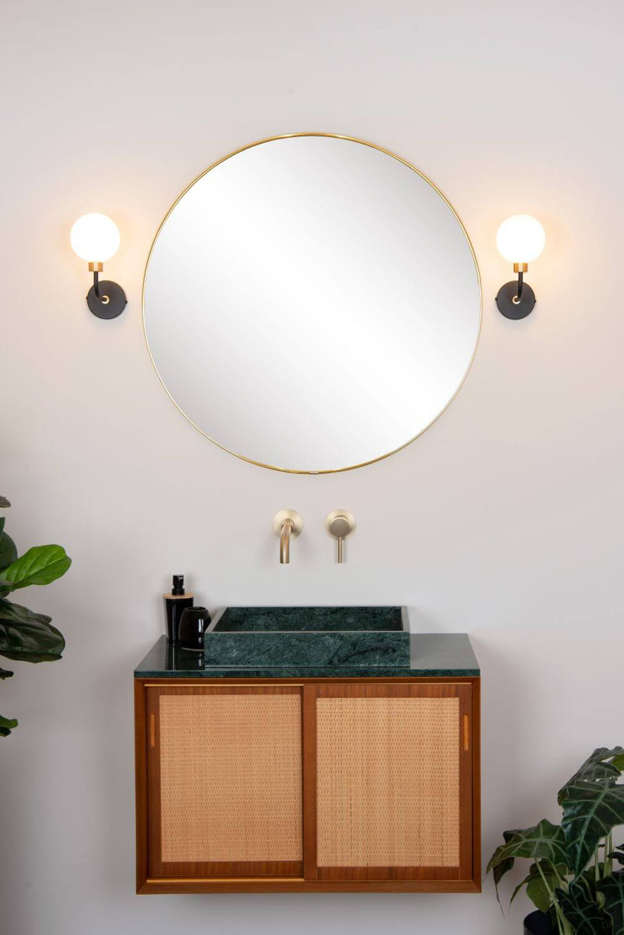 Vue rapprochée de la salle de bain : miroir rond, vasque verte et appliques murales éteintes.