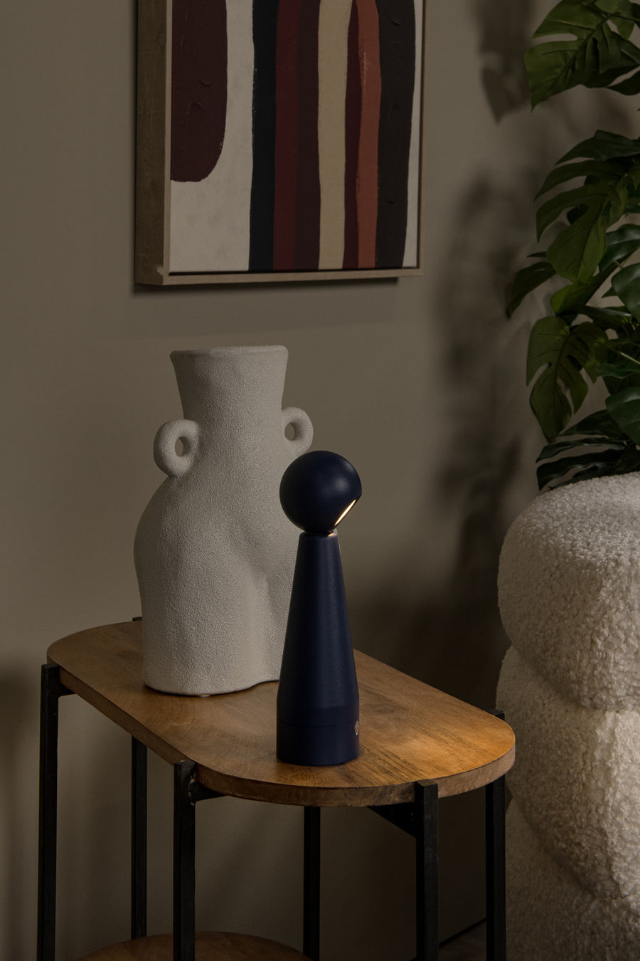 Lampe bleue allumée sur une table en bois auprès d'un vase blanc texturé.