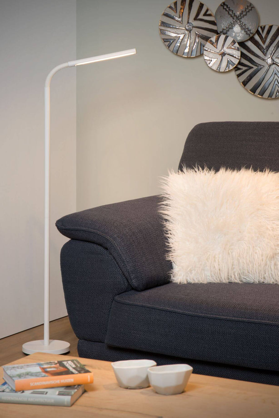 Lampadaire blanc installé près d'un canapé, avec coussin et livres sur table basse
