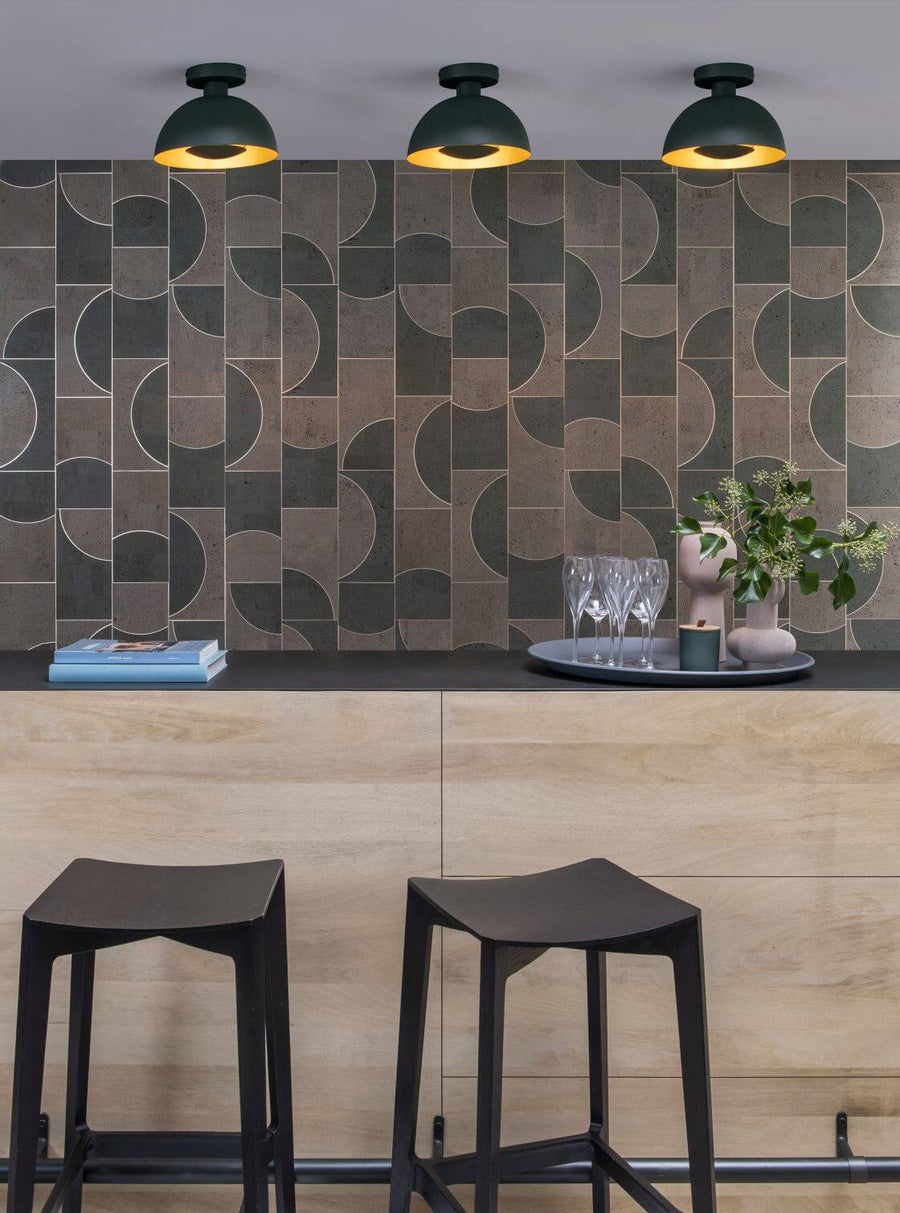 Vue rapprochée de trois luminaires verts au-dessus d’un comptoir en bois et carrelage graphique.