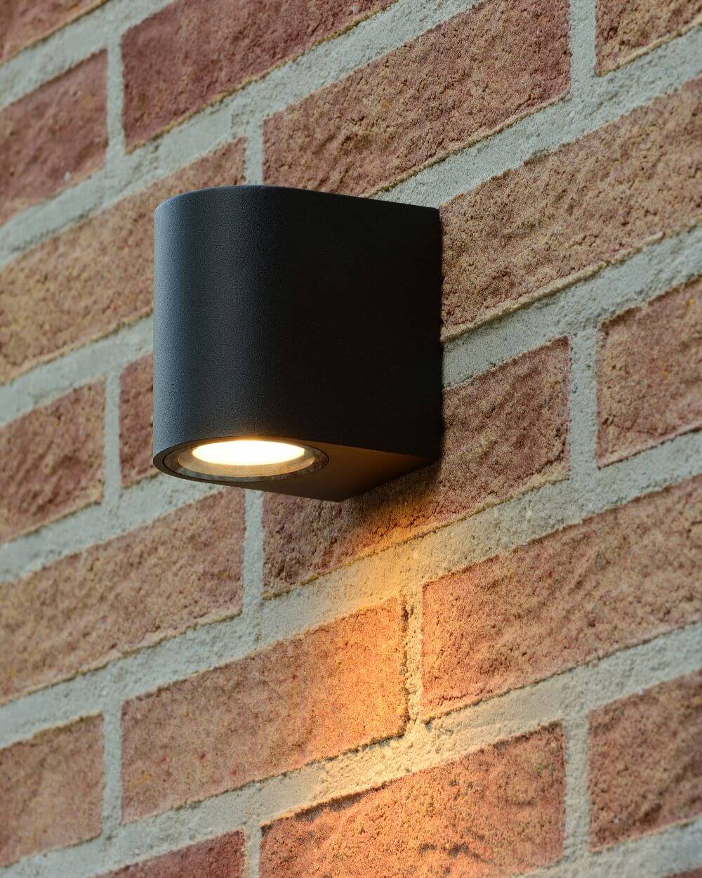 Mise en ambiance nocturne sur mur de briques rouges, halo chaud projeté vers le bas