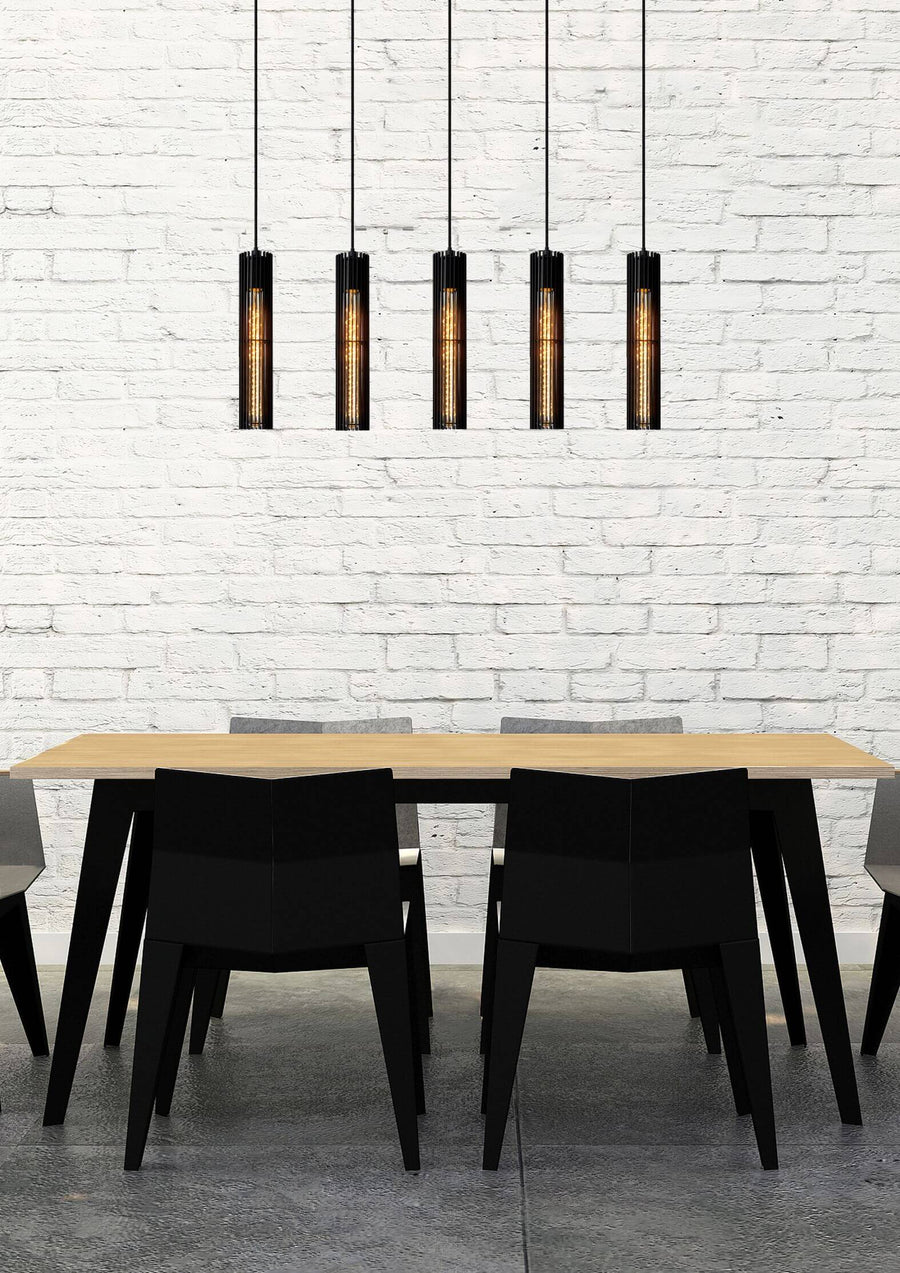 Suspension à cinq lumières noires installée au-dessus d'une table à manger devant un mur de briques.