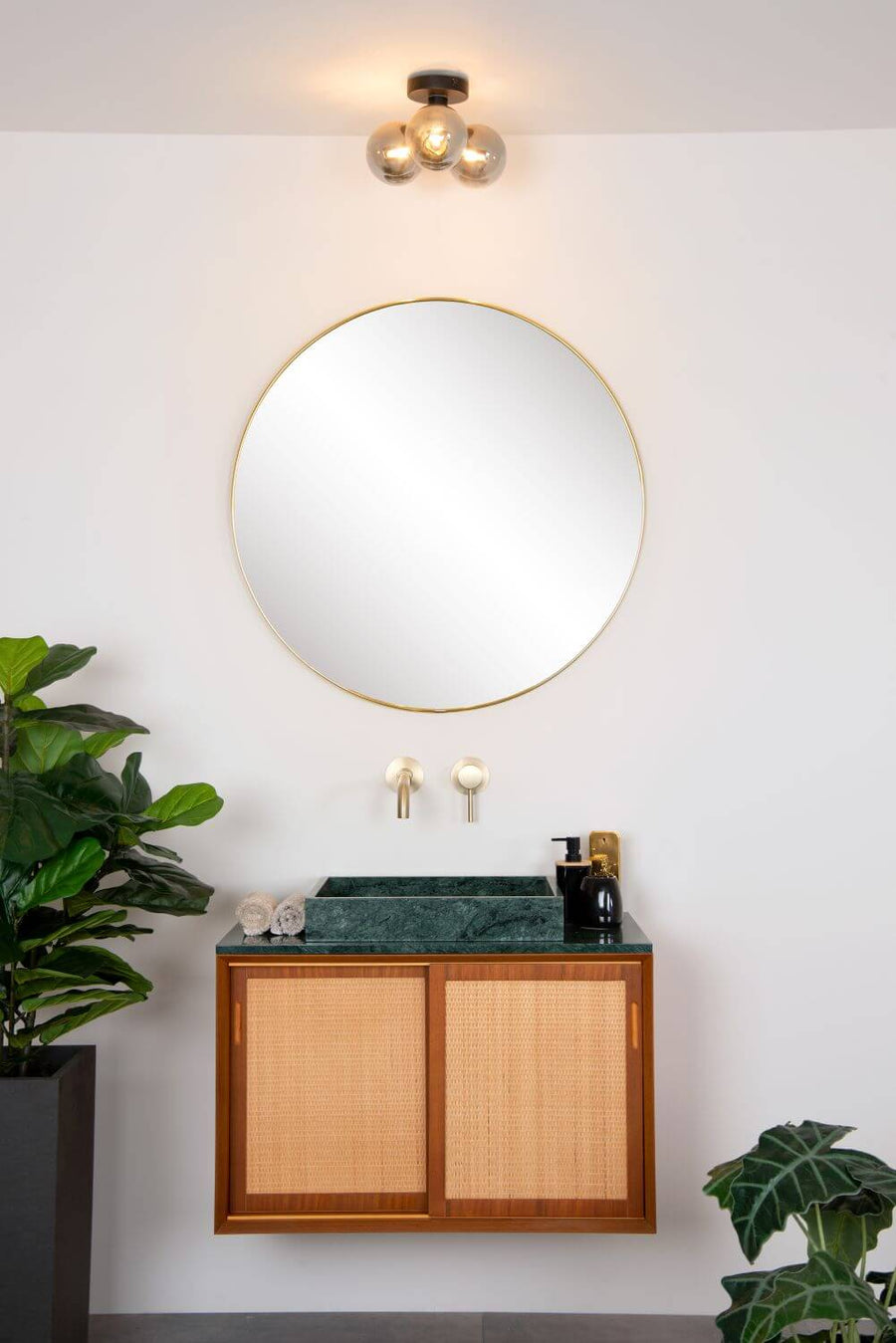 Vue rapprochée du luminaire allumé éclairant le miroir doré et le meuble vasque en rotin.