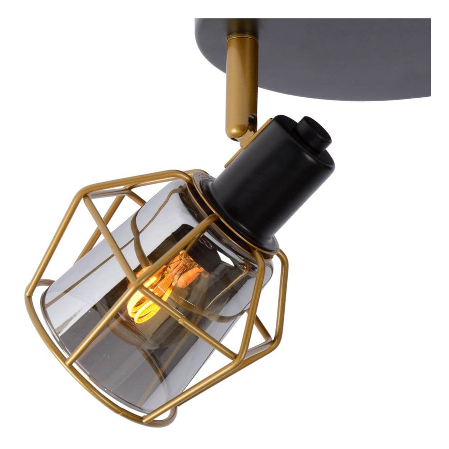 Détail rapproché d'un spot : cage métallique dorée, douille noire et verre fumé.