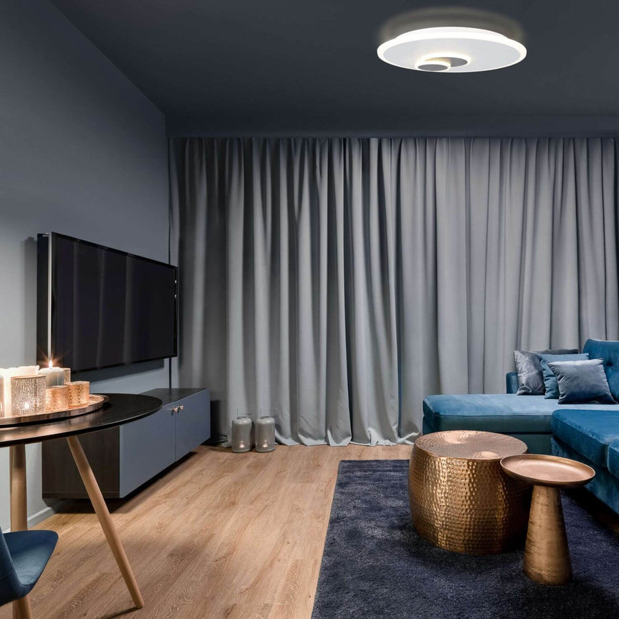 Plafonnier blanc allumé dans un salon sombre aux rideaux gris