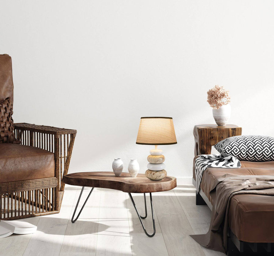 Scène de vie avec lampe à poser sur table basse, fauteuil en rotin et lit.