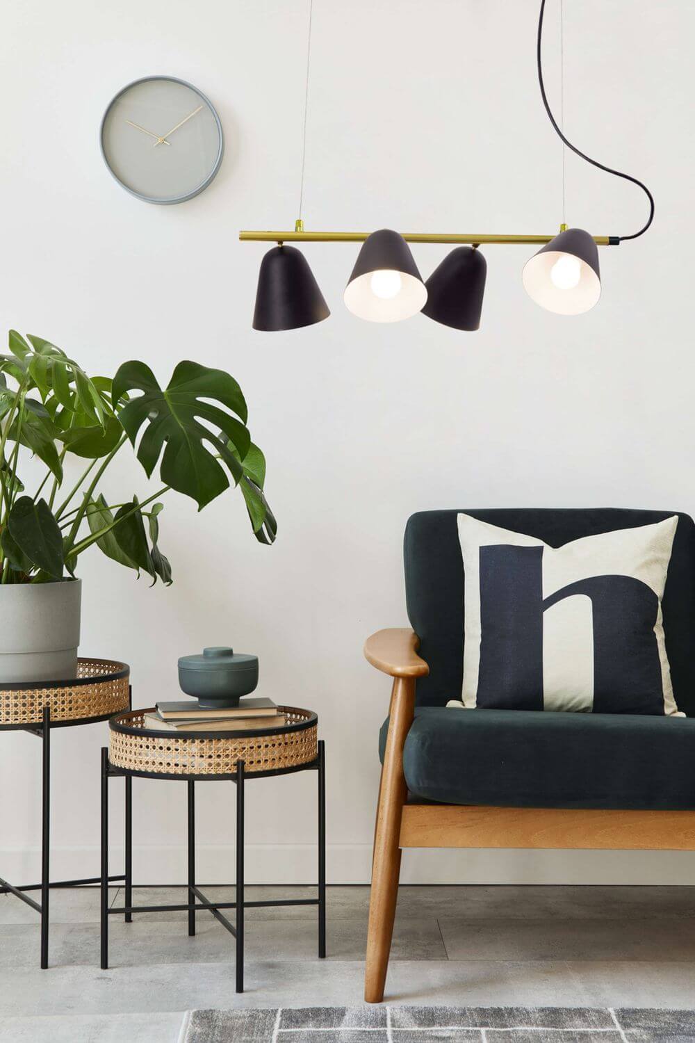 Mise en ambiance : luminaire suspendu au-dessus de tables d'appoint, fauteuil, plante et horloge murale.