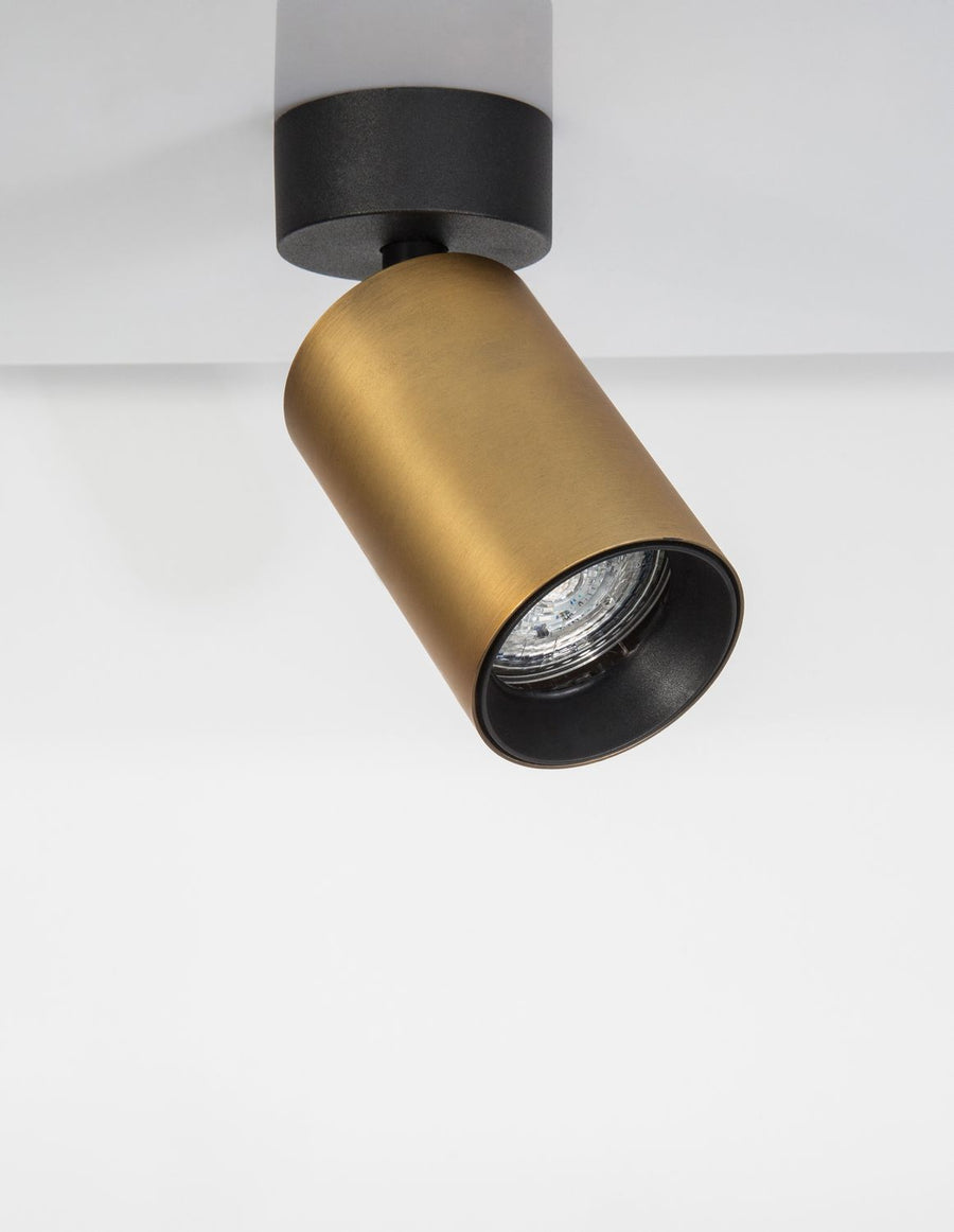 Spot cylindrique doré orientable monté au plafond blanc, incliné vers le bas