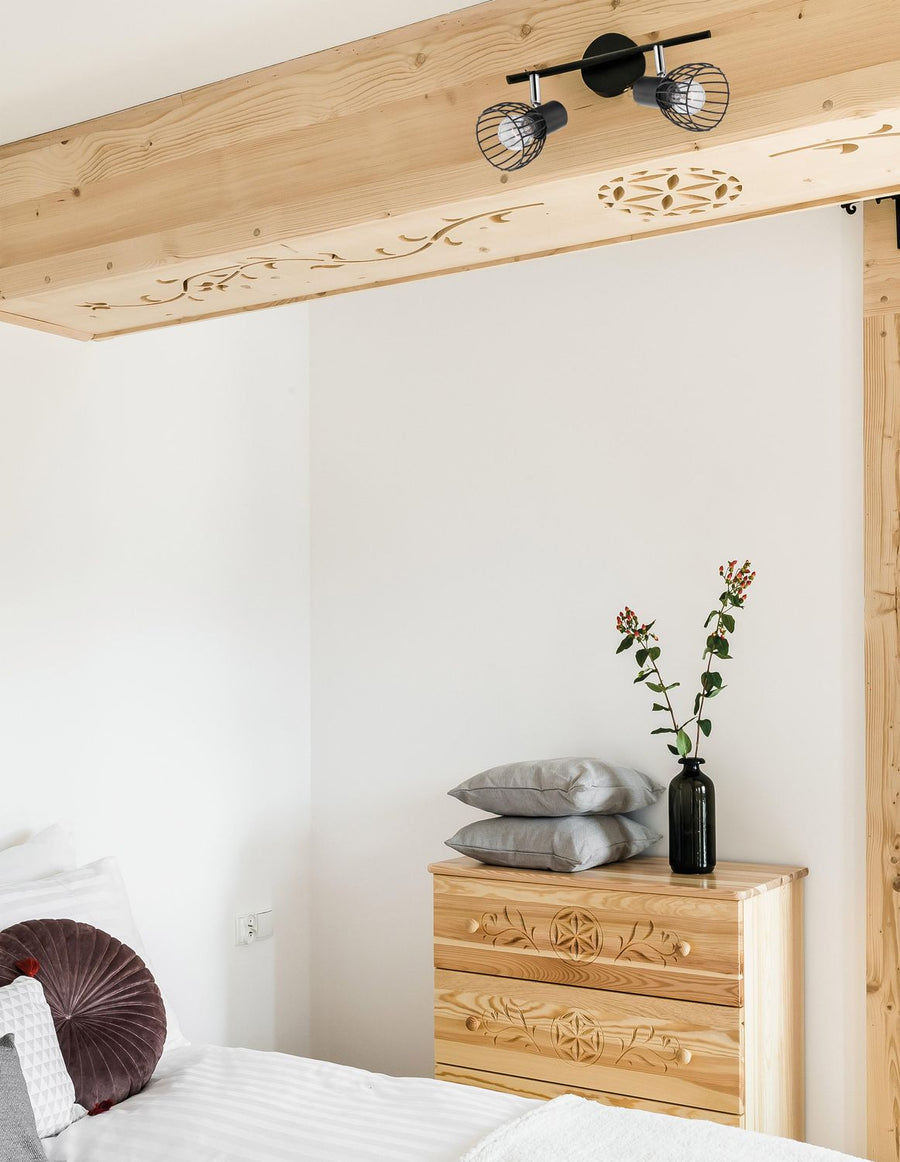 Plafonnier noir à deux cages installé sur poutre en bois dans une chambre.