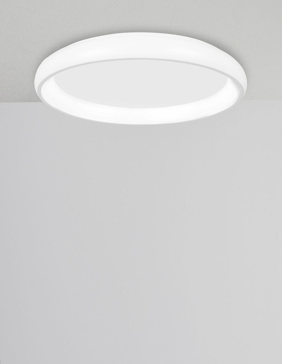 Plafonnier rond blanc allumé au plafond dans une pièce claire et épurée