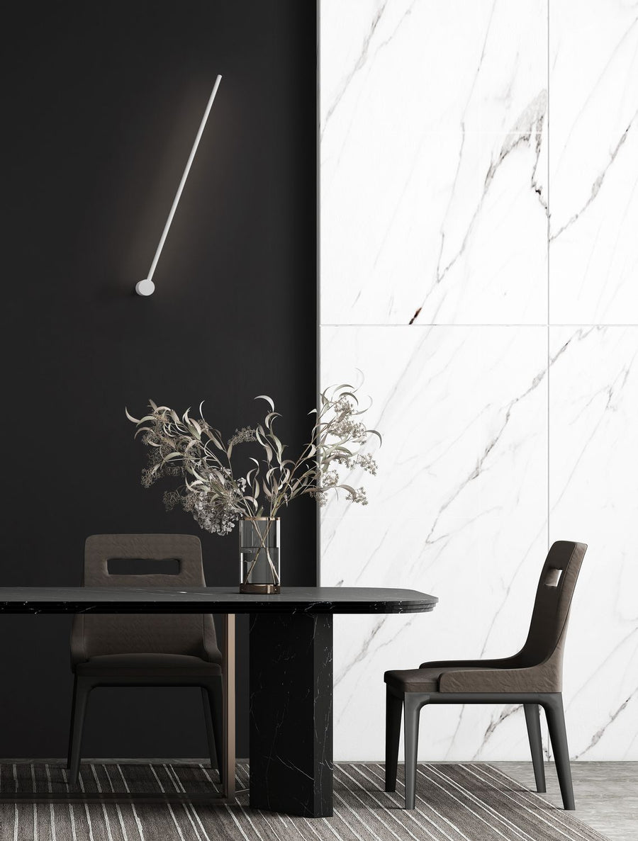 Applique murale blanche inclinée éclairant un mur noir au-dessus d'une table à manger